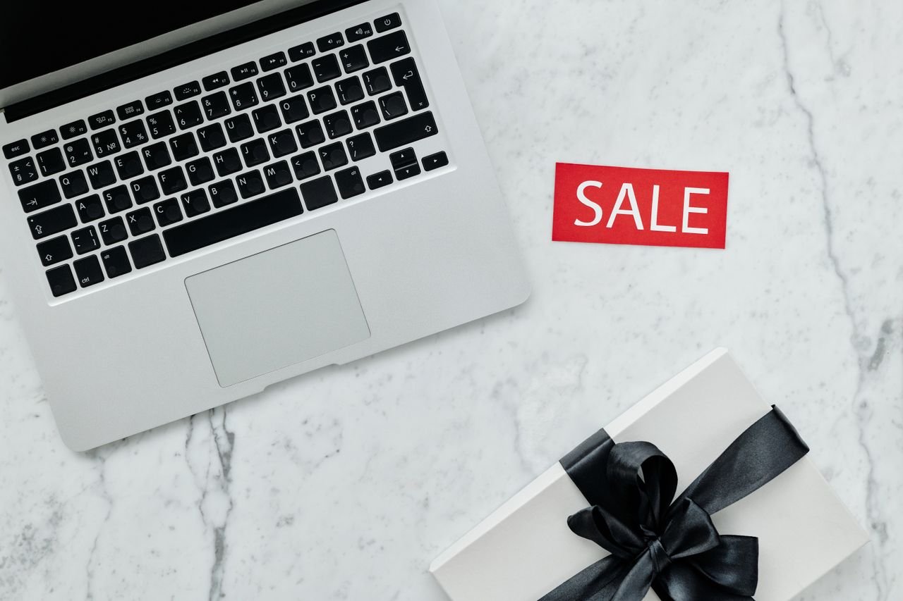 service-01 Top-down view of a laptop and gift with a sale sign on marble background.