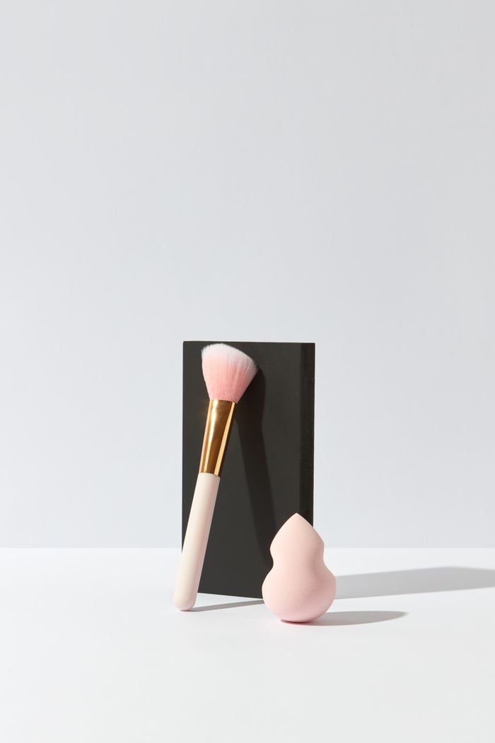 service-06 Elegant minimalist composition of a makeup brush and sponge blender on a white surface with a black background.