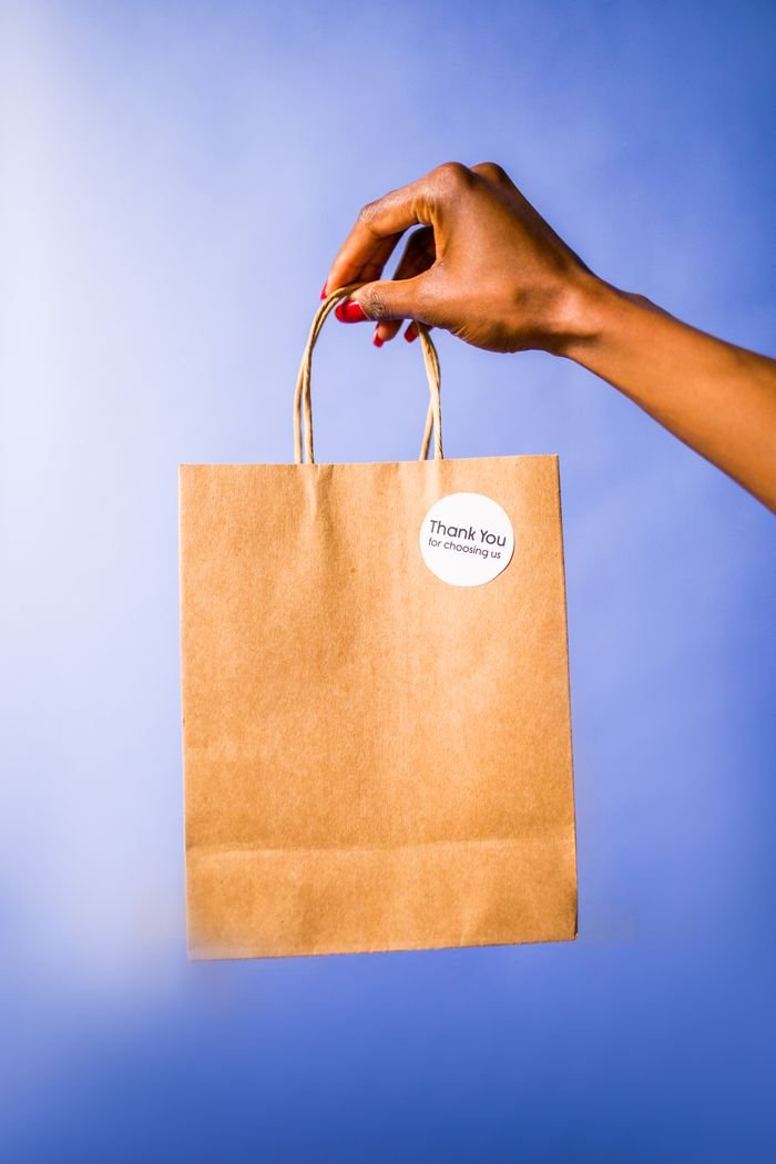 service-03 A hand holds a thank you paper bag against a vibrant blue background.